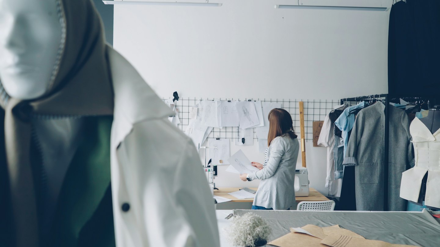 Fashion designer reviewing sketches and patterns at her studio workstation.